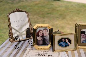 Gold-framed wedding photos and marriage certificate displayed on striped table at reception.