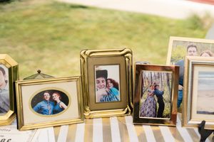 Gold-framed photos of a couple displayed on a striped table at an outdoor wedding reception.