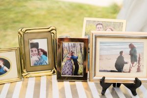 Collection of framed engagement and couple photos displayed on striped table at wedding reception.