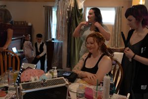 Bride laughing while getting hair and makeup done by stylists in preparation for her wedding day.