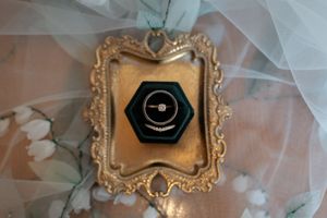 Diamond engagement ring displayed in a dark green hexagonal velvet box with ornate gold frame.
