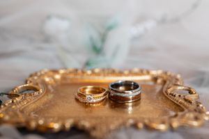 Two gold and silver wedding rings displayed on ornate golden tray with floral background.