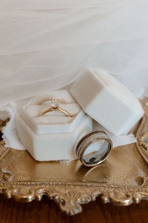 Wedding rings displayed in white velvet hexagon box on ornate gold tray with bridal veil.