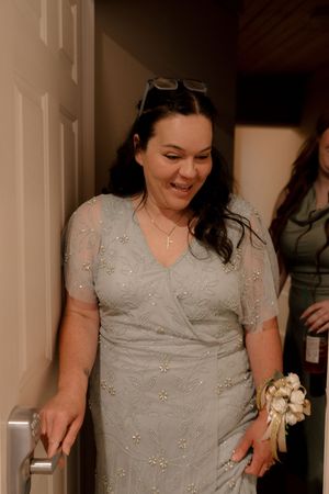 Woman in elegant silver beaded dress with wrist corsage smiles while descending stairs at a wedding.