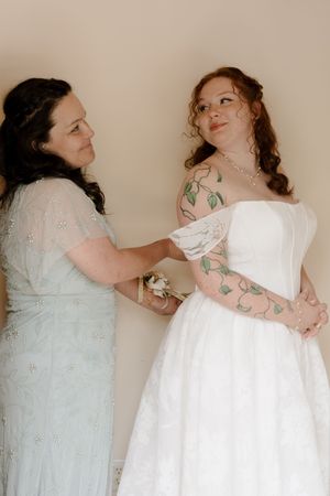 Mother helps bride with tattoos adjust her white strapless wedding gown before the ceremony.