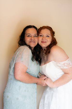 Bride in white off-shoulder gown shares a warm embrace with her mother in a light blue dress before the wedding.