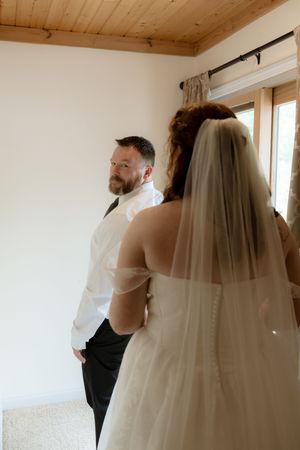 Groom in white shirt looks back at bride in white veil during emotional first look wedding moment indoors.