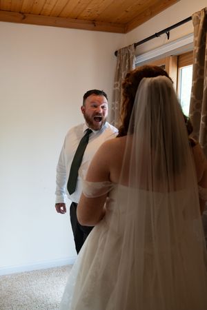 Man in white shirt and green tie reacts with open mouth surprise seeing bride in white wedding gown.