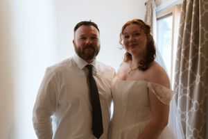 Bride in off-shoulder gown and groom in white shirt and dark tie posing indoors.