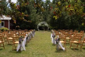 Outdoor wedding ceremony setup with wooden chairs, floral aisle decor, and circular arch on lawn.