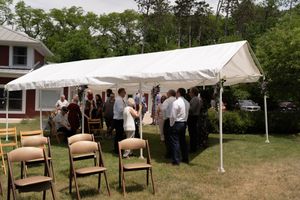 Outdoor wedding reception under white tent with guests mingling on sunny green lawn.