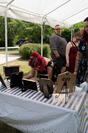 Red-haired woman browses wedding reception gift table under a white tent at an outdoor celebration.