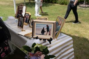 Outdoor wedding memory table displaying framed couple photos on a striped tablecloth with floral decorations.