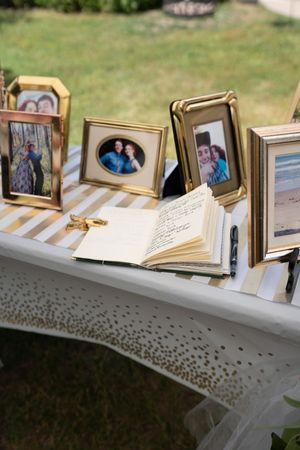 Wedding guest book table with gold frames, photos of couple, and open sign-in book outdoors.