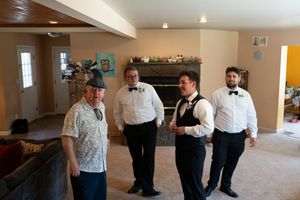 Groom and groomsmen in white shirts and bow ties share a lighthearted moment indoors before the wedding ceremony.