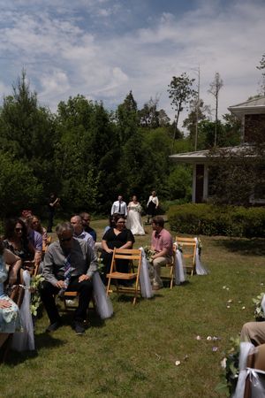 Guests seated in wooden chairs watching bride walk down aisle at outdoor wedding.