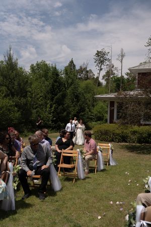 Wedding guests seated in wooden chairs along a flower-lined aisle at an outdoor garden wedding ceremony.