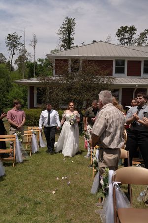 Newlywed couple walks back down aisle after outdoor wedding ceremony as guests celebrate with petals.