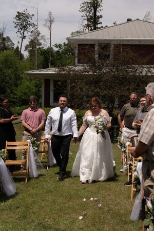 Newlywed couple walks down the aisle at an outdoor wedding ceremony surrounded by cheering guests.