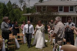 Newlyweds walk down the aisle at outdoor backyard wedding ceremony as guests celebrate around them.