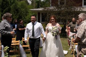 Newlyweds walk joyfully down outdoor aisle hand-in-hand after garden wedding ceremony.