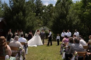 Outdoor wedding ceremony with bride and groom at altar surrounded by seated guests and lush trees.