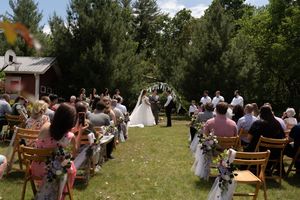 Guests seated outdoors watching bride and groom exchange vows under floral arch in garden.