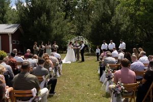 Outdoor wedding ceremony in a garden setting with guests seated as bride and groom exchange vows beneath a floral arch.