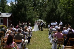 Aerial view of outdoor wedding ceremony with guests seated on chairs facing bride and groom at floral arch.