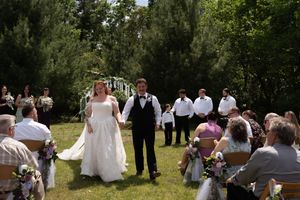 Bride and groom walk hand in hand down outdoor aisle at garden wedding ceremony surrounded by guests.