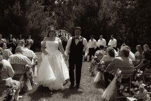Black and white photo of a newlywed couple walking down the aisle at an outdoor wedding ceremony.