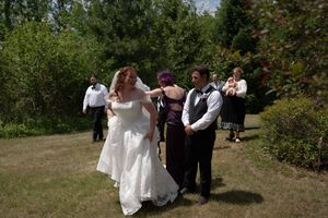 Bride in white gown dancing with groom outdoors at wedding reception on sunny day with guests in background.