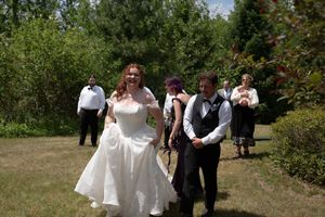 Bride and groom walk together through a sunny garden with wedding guests in the background.
