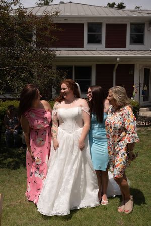 Bride in white off-shoulder gown stands with three bridesmaids in colorful dresses outdoors on a sunny wedding day.
