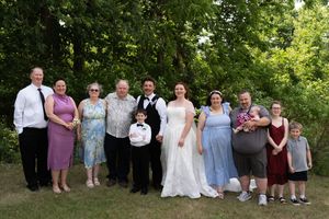 Wedding family portrait with bride, groom, and relatives posing outdoors among green trees.