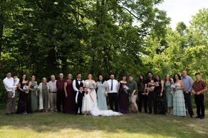 Large wedding party group photo with bride, groom, bridesmaids in sage green, and guests outdoors.