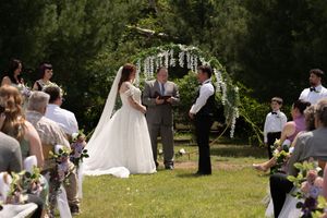 Bride and groom exchange vows at an outdoor wedding ceremony beneath a floral arch surrounded by guests.
