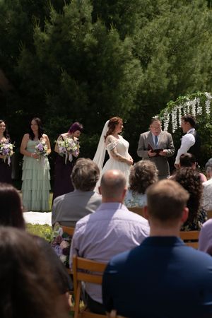 Outdoor wedding ceremony with bride, groom, officiant, and bridesmaids before seated guests.