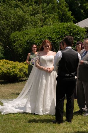 Bride in elegant lace gown with long train exchanging vows with groom at outdoor ceremony.