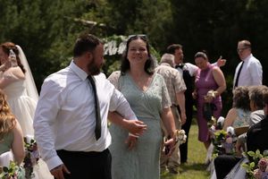 A smiling woman in a green beaded dress walks with a man in a white shirt at an outdoor wedding.