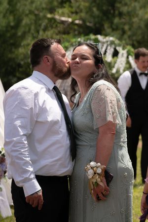 Couple sharing a romantic kiss at outdoor wedding celebration, woman wearing sage green lace dress.