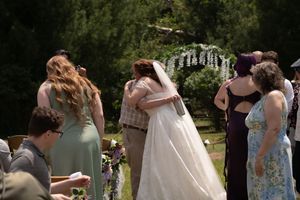 Bride in white gown and veil sharing an emotional hug at outdoor wedding ceremony altar.