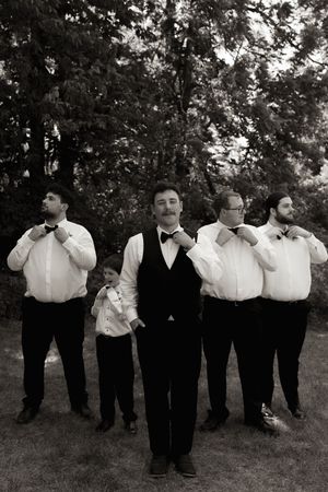 Black and white photo of groom and groomsmen adjusting bow ties in a stylish outdoor wedding portrait.