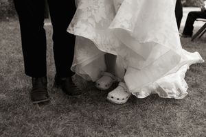 Black and white close-up of bride wearing white Crocs and groom in dress shoes at wedding.