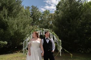 Bride and groom holding hands under a wisteria arch in a lush green garden on their wedding day.