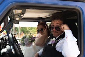 Bride and groom wearing sunglasses smile together inside a vintage blue truck after wedding.