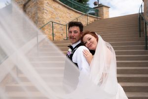 Bride in white gown and veil embraces groom in black suit on outdoor stone staircase wedding portrait.