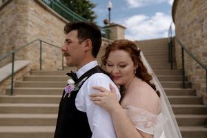 Bride in white veil embraces groom from behind on stone staircase in tender wedding portrait.