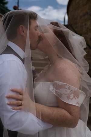 Bride and groom share a romantic kiss under a flowing white veil outdoors on their wedding day.
