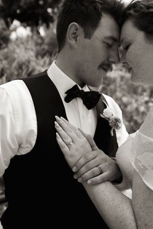 Black and white wedding photo of bride and groom touching foreheads, showing off wedding rings.